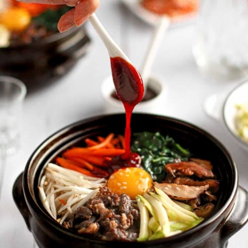 Dolsot bibimbap composed of rice, marinated beef, seasoned vegetables, one egg. sauce made out of gochujang.