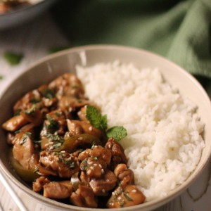 Asian style chicken marinated in a lime and hoisin marinade, cooked with mushrooms, green capsicums, onions and served with rice, mint and sesame seeds in a deep plate.