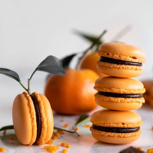 macarons with smooth and shiny shells filled with madarin chocolate ganache piled up on a table.