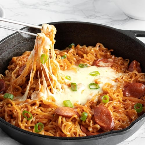 cheese buldak ramen with wurstel sausage and melted mozzarella, chopsticks digging in the melted cheese.