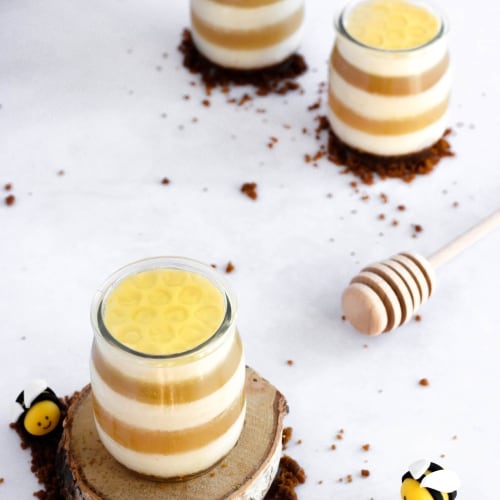 honeycomb-shaped coconut pineapple cheesecakes made with layers of coconut cheesecake and pineapple juice jelly sitting on a table with homemade bees around.