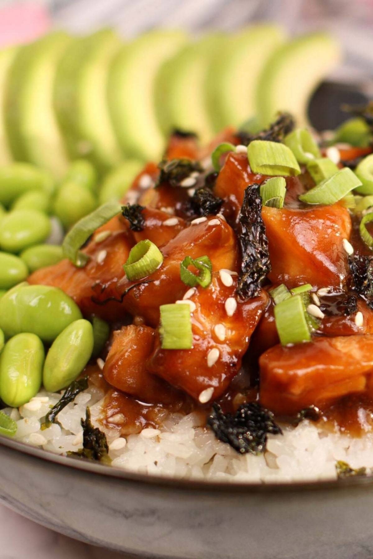 The marinated salmon is coated with an incredibly delicious homemade teriyaki sauce and served on top of white rice with avocado and edamame.
