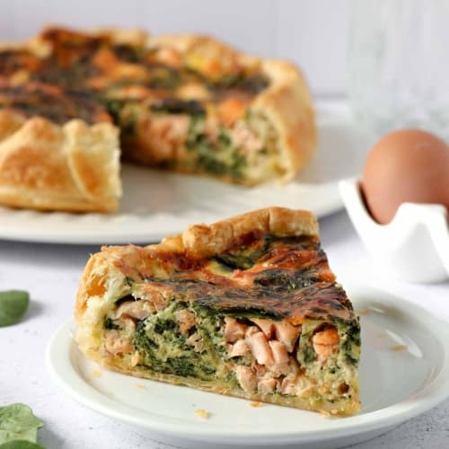 a slice of salmon and spinach quiche on a plate.