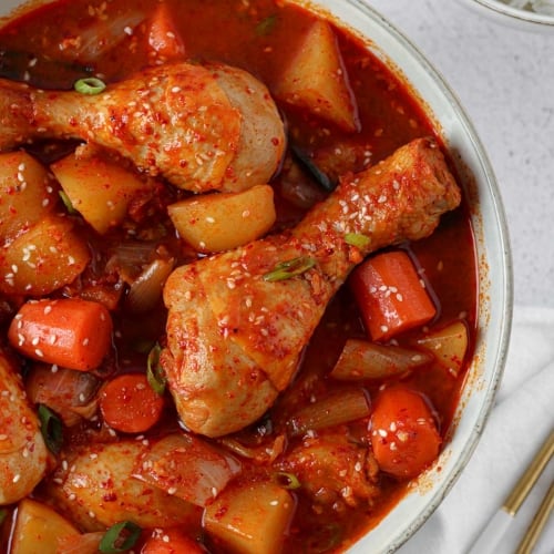dakdoritang korean spicy chicken stew in a bowl with chopsticks and a bowl of rice aside.