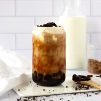 a glass with boba, milk tea, cheese foam and some crushed oreo cookies