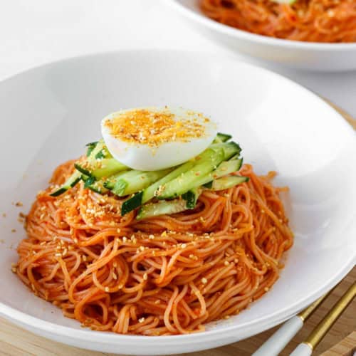 Bibim guksu spicy cold noodles topped with cucumber and boiled egg.