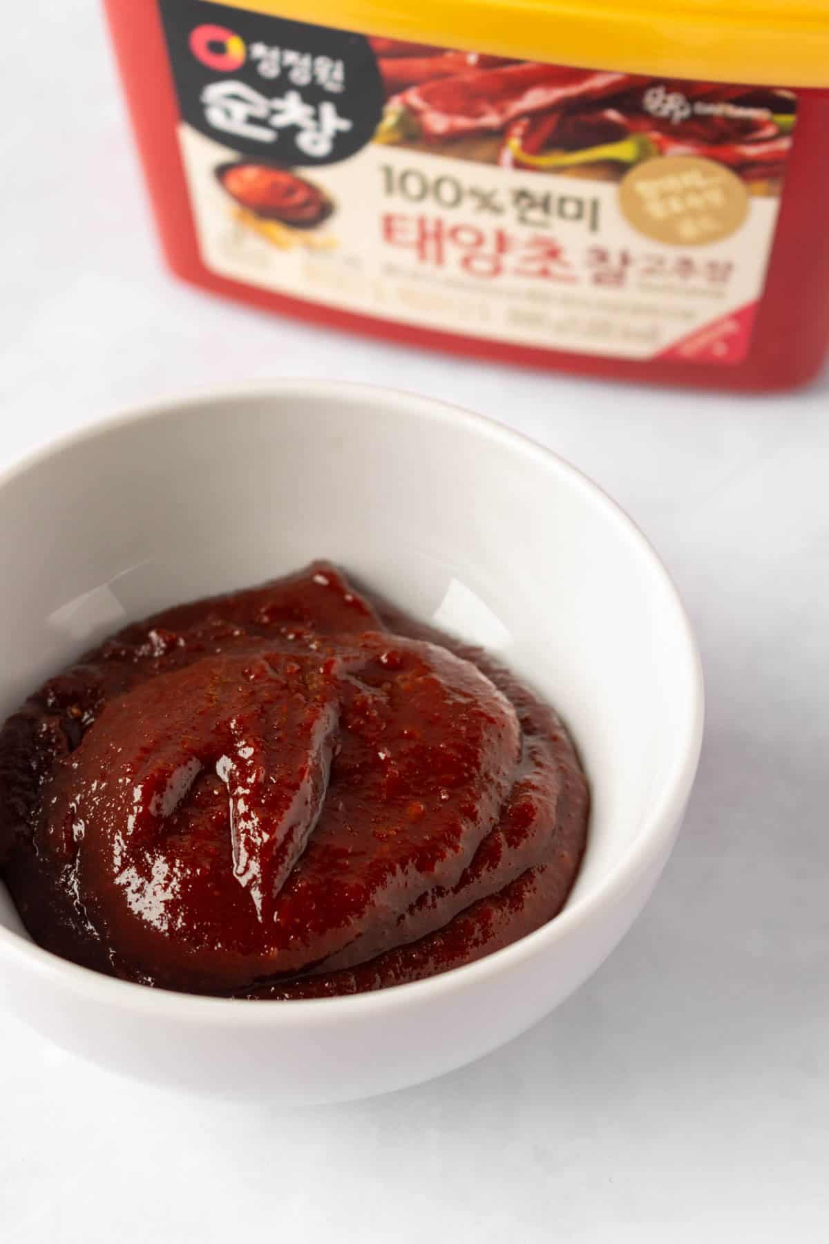 Korean gochujang tub beside a small bowl of red fermented chili paste.